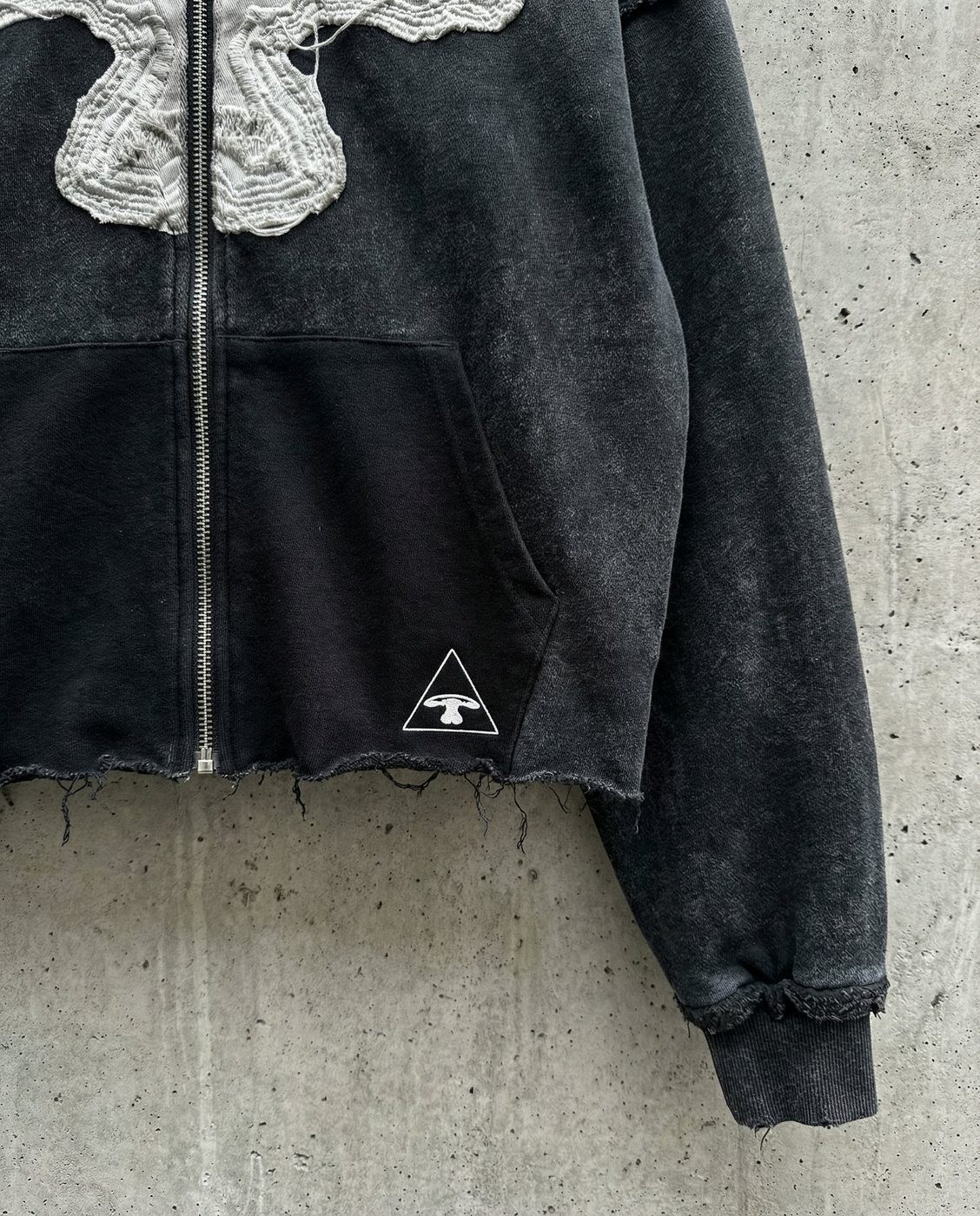 Pormenor da frente do zip-up 5LOOP: aplicação desfiada e etiqueta triangular