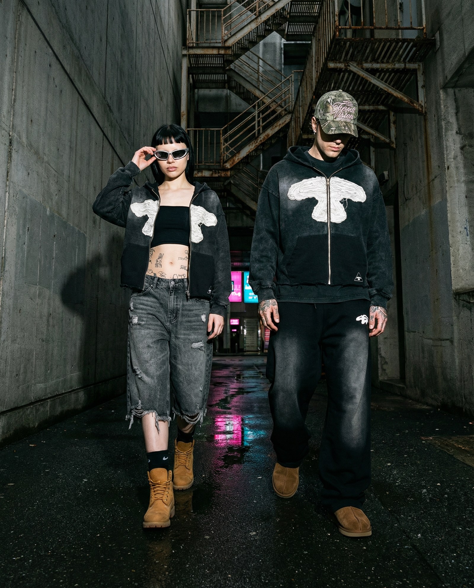 Streetwear: dois modelos com casacos zip-up num beco de betão à noite