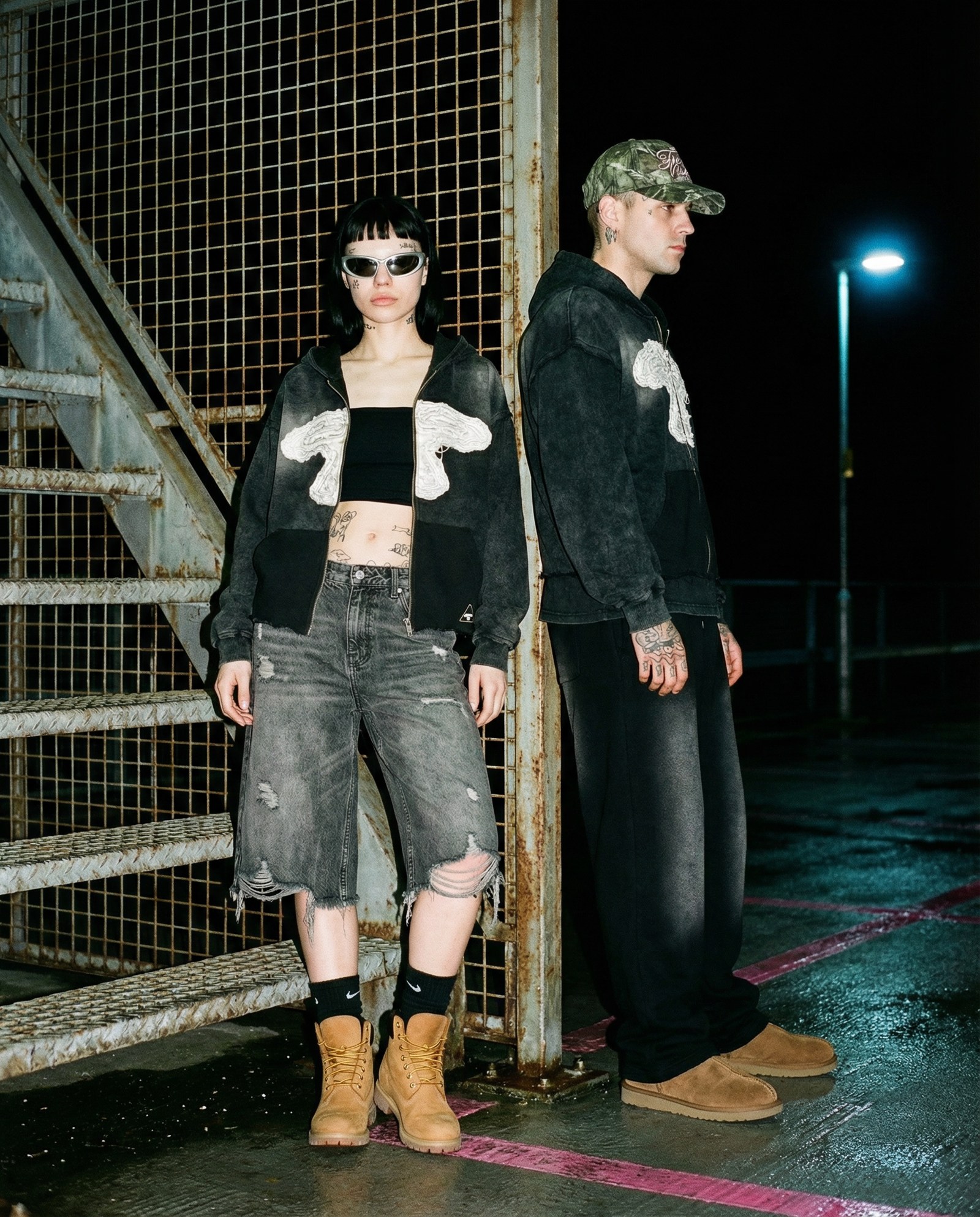 Dois modelos com o zip-up 5LOOP junto a uma escada metálica, à noite