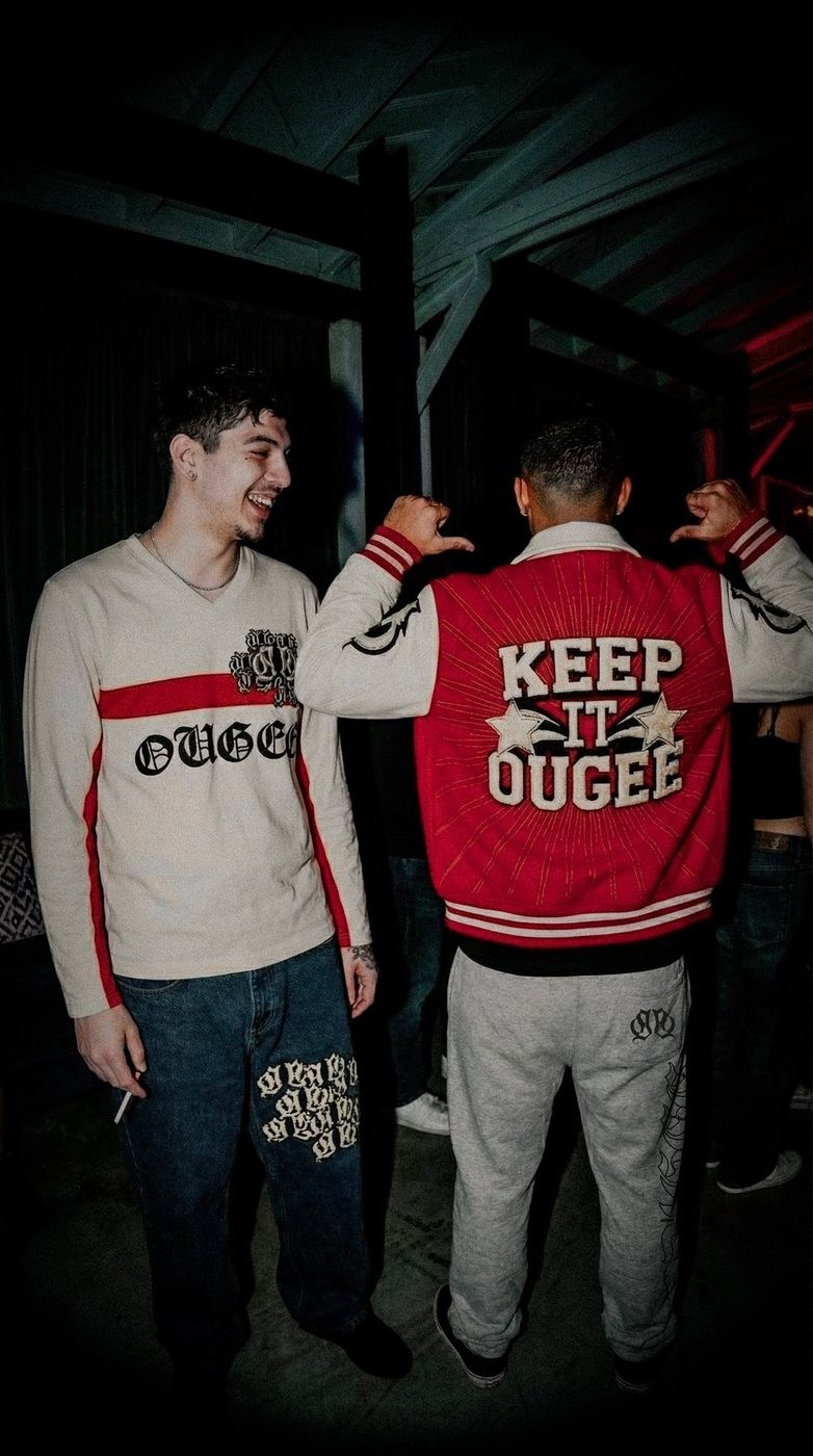 Dois rapazes numa festa com peças OUGEE: camisola creme e casaco vermelho Keep It Ougee