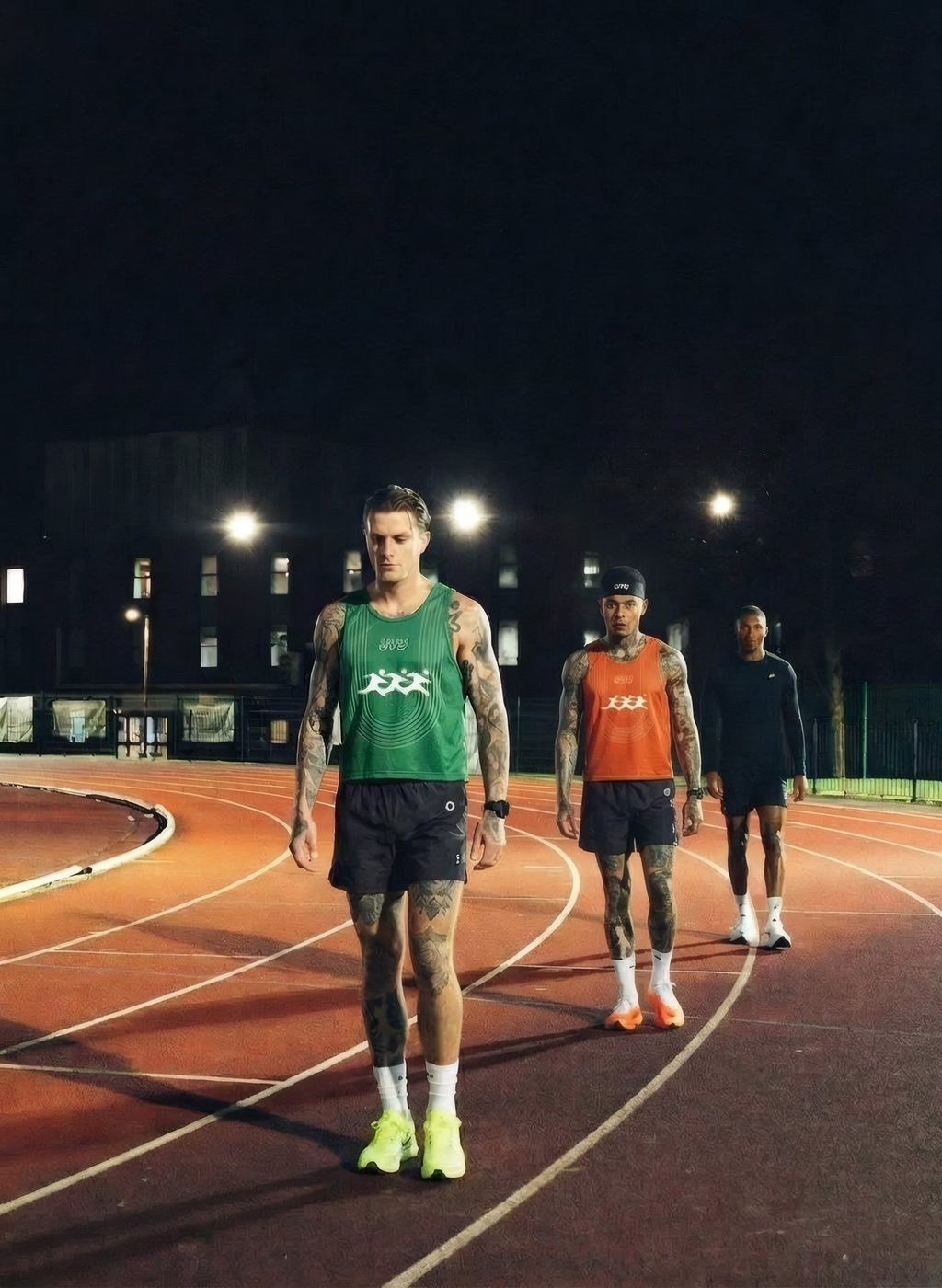Três corredores de pé numa pista de atletismo à noite, com camisolas UVU